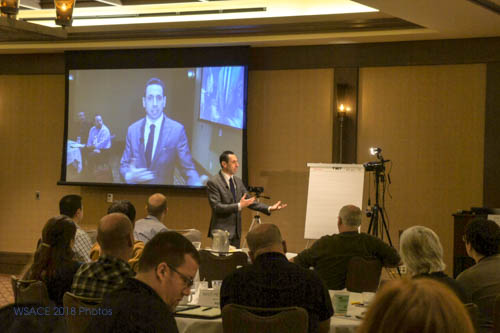 Male presenter delivers media training presentation to seated audience in conference room.